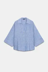 Camisa celeste confeccionada en hilatura con lino, de corte holgado. Tiene cuello solapa, escote pico, manga tres cuartos y bajo asimétrico. Cierre frontal con botones.