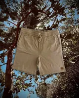 Bermuda color beige con cintura elástica ajustable con cordón, bolsillos laterales y un pequeño logo en la parte inferior de la pierna derecha.