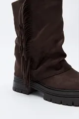Bota de caña media con flecos laterales, confeccionada en material con textura tipo gamuza. Presenta una silueta relajada y suela robusta con base dentada.