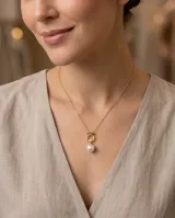 Collar de plata 925 con baño de oro, compuesto por una cadena fina y un dije circular que sostiene una perla natural y una pequeña circonia brillante.