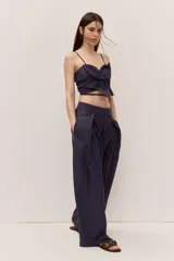 Pantalón azul marino de tiro alto con cintura ancha y pliegues frontales que aportan volumen y una caída suelta y fluida, con diseño envolvente en la cadera y bolsillos laterales.