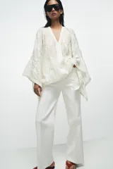 Blusa tipo capa de algodón con escote en pico y mangas largas amplias. Presenta bordados florales a tono en toda la prenda, bajo asimétrico y cierre frontal con botones.