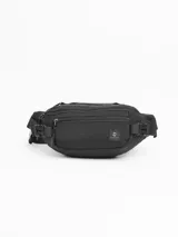 Riñonera urbana de diseño funcional en color negro. Cuenta con dos compartimentos frontales con cierre, un bolsillo trasero oculto de seguridad, manija superior de transporte y correa ajustable con cierre de broche. Incluye parche con logo de la marca en el frente.