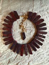 Collar de jaspe rojo natural en tonos bordeaux y rojo profundo, con piezas rectangulares dispuestas en fila y cadena de extensión dorada con dije colgante.