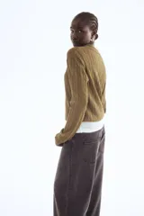 Sweater de punto color verde oliva, con cuello polo, tapeta de dos botones y manga larga. Presenta un tejido con diseño de trenzas verticales a lo largo del cuerpo y puños y bajo acanalados.