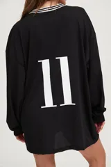 Camiseta negra oversize de manga larga con cuello en V blanco y logo en el pecho.