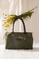 Bolso amplio de gamuza verde musgo con manijas largas de cuero marrón, bolsillos laterales, cierre posterior y compartimento principal con cierre.