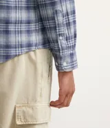 Camisa de franela de manga larga con estampado de cuadros en tonos azul y gris. Tiene cuello camisero y cierre frontal con botones.