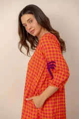 Vestido largo de corte holgado en tonos naranja y fucsia con estampado de cuadros vichy. Presenta cuello en V con detalles bordados, mangas tres cuartos y bordados decorativos de palmeras en contraste en las mangas.