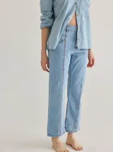 Jean de corte recto confeccionado en denim azul oscuro, con costuras a la vista en color rojo contrastante. Presenta un diseño de tiro alto con bolsillos frontales y cierre de botón.