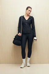 Campera deportiva negra de calce entallado, con cierre frontal completo, capucha integrada y mangas largas con puños envolventes. Presenta costuras estratégicas que estilizan la silueta y bolsillos laterales funcionales.