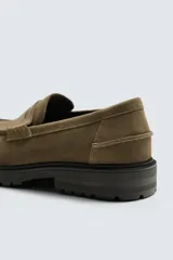 Mocasín de vestir para hombre, confeccionado en piel con acabado de serraje en color marrón oscuro. Presenta un diseño clásico con detalle de antifaz en el empeine, horma redonda y una suela track robusta de goma.