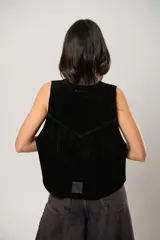 Chaleco de cuero descarne color tostado, con diseño oversize y terminación en picos. Presenta tachas metálicas a lo largo de la abertura frontal y flecos en la espalda.