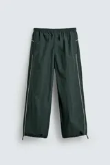 Pantalón jogger de corte relajado confeccionado en tejido técnico de color verde oscuro. Presenta cintura elástica con cordón interior, bolsillos laterales con cierre y bajo ajustable con elástico. Incluye detalles de líneas en contraste a lo largo de las piernas.