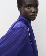 Blusa de poliéster color azul, con cuello alto, lazada integrada, cierre lateral con botones y mangas largas abullonadas con puños ajustados.