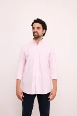 Camisa de corte clásico confeccionada en algodón, con diseño de rayas verticales finas en color rosa sobre fondo blanco. Presenta cuello abotonado, cierre frontal con botones, mangas largas con puños abotonados y un bolsillo en el pecho con el logo de la marca bordado.