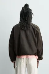 Cazadora de corte cropped confeccionada en algodón con acabado encerado. Presenta cuello subido, cierre frontal con cremallera oculta por solapa con botones a presión, bolsillos de plastrón con solapa en el delantero y bajo ajustable con elástico interior.
