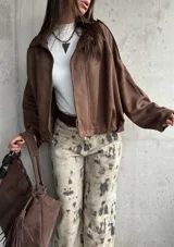 Campera tipo bomber de gamuza color chocolate, con diseño oversize, mangas amplias y apliques decorativos en los hombros. Cuenta con cierre frontal y forro interior.