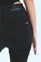 Jean negro de tiro medio alto, corte oxford con botamanga ancha y tajo. Cierre frontal con cinco botones metálicos.