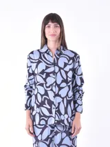 Camisa de manga larga con cuello clásico y cierre frontal con botones. Presenta un estampado abstracto en tonos celeste y negro.