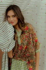 Blusa de algodón con estampado floral multicolor, con detalles en tela a cuadros verde y blanca en el cuello en V, la pechera y los bordes de las mangas cortas.