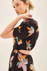 Vestido corto de cuello redondo con estampado floral multicolor sobre fondo negro. Presenta mangas cortas con detalle fruncido en los hombros y aberturas laterales en la cintura.