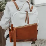 Mochila de cuero vacuno color marrón y blanco, con bolsillo frontal con cierre, dos bolsillos laterales, interior forrado con bolsillo con cierre y bolsillo para celular. Las correas son removibles.