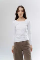 Remera básica de manga larga en color gris melange, confeccionada en algodón suave. Presenta un diseño de cuello redondo y un detalle de etiqueta decorativa en el puño.