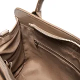 Cartera tipo tote de textura granulada color taupe, con manijas cortas y correa larga ajustable extraíble. Presenta un bolsillo frontal con cierre metálico y el logo de la marca en aplique metálico.
