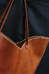 Cartera de cuero color marrón chocolate con manijas largas y borde superior en corte en V. Diseño amplio y liviano, con terminaciones artesanales y costuras contrastantes en todo el contorno.