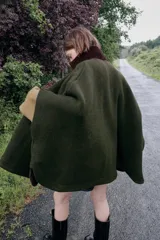Capa de punto color verde oscuro con cuello subido de pana en color marrón. Presenta cierre frontal con cremallera metálica y diseño holgado.