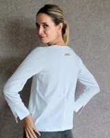 Remera blanca de manga larga con cuello en V y costuras decorativas en contraste. Incluye un lazo ajustable en el cuello con herraje metálico circular.