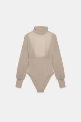Body de cuello subido con mangas largas abullonadas y puños elásticos. Presenta un diseño combinado con paneles de tela semitransparente en la parte superior y tejido opaco en la parte inferior.