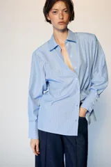 Camisa de manga larga con cuello solapa y hombreras. Presenta un diseño de rayas verticales en tonos azul y blanco, con cierre frontal de botones y puños anchos.