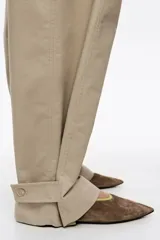 Pantalón de algodón color beige, de corte barrel ancho con tiro bajo. Presenta bolsillos en costuras delanteros y con vivo en la parte trasera. El bajo de la pierna tiene trabillas para ajustar el volumen.