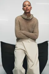Jersey de punto calado color beige, con cuello alto vuelto y manga larga, confeccionado en lino.