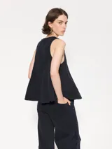 Top sin mangas color celeste claro, confeccionado en gabardina, con escote delantero ajustable mediante cordón y ojalillos. Presenta recortes triangulares que generan vuelo en la parte inferior.