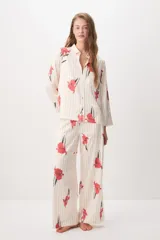 Pijama de satén compuesto por una camisa de manga larga con botones y un pantalón largo, ambos de color crudo con estampado de rayas verticales negras y flores rojas.