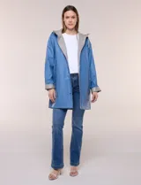 Pilot engomado impermeable color azul, de corte recto estilo trench con acabado resistente al agua. Cuenta con capucha integrada, cierre frontal con broches a presión, bolsillos laterales con ojal y forro interior de tela estampada a cuadros visible en la solapa y los puños.