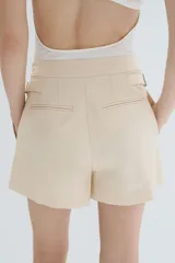 Short de mezcla de algodón y lino color beige, con pinzas delanteras, raya marcada al frente y ajuste con hebillas metálicas en los laterales.