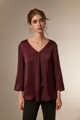 Blusa de satén color bordó con cuello en V y mangas tres cuartos. Presenta un diseño holgado con un pliegue central en el frente.