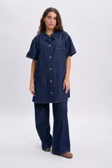 Vestido corto de jean azul oscuro, de manga corta, con cuello camisero, cierre frontal de botones metálicos y un bolsillo aplicado en el pecho.