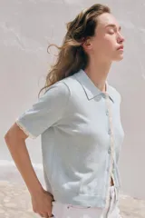 Chaqueta de punto celeste de manga corta con cuello polo, cierre frontal con botones y detalles de puntilla en color beige en la botonera y los puños.