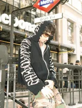 Hoodie con cierre frontal, confeccionado en tejido de punto 100% algodón. Es una prenda reversible con diseño de estampado gráfico en mangas y capucha, y presenta detalles de roturas intencionales en puños, ruedo y bolsillos.