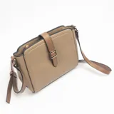 Bandolera de cuero sintético color camel, con diseño estructurado, cierre superior y solapa decorativa con hebilla metálica dorada. Incluye correa larga ajustable para llevar al hombro o cruzada.