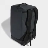 Bolso de viaje tipo duffel bag, color gris oscuro/negro, con múltiples compartimentos, bolsillo independiente para calzado y asas de mano, además de correa ajustable para llevar al hombro. Presenta detalles de cinchas y un parche con logo en el frente.