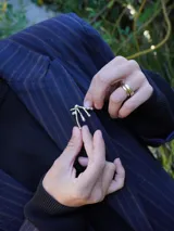 Pin plateado con forma abstracta de ramas con gotas.