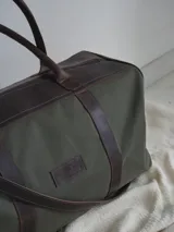 Bolso de lona color verde militar con detalles en cuero marrón. Tiene doble asa de mano y correa de hombro ajustable y extraíble.