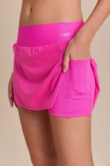 Pollera deportiva color rosa fucsia, con estampado en relieve de texto. Es de corte corto con ruedo redondeado y cuenta con shorts internos.