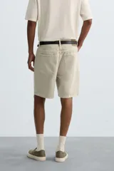 Bermuda de denim de algodón color beige claro, de corte regular fit y largo hasta la rodilla. Presenta cinco bolsillos y cierre frontal con cremallera y botón.